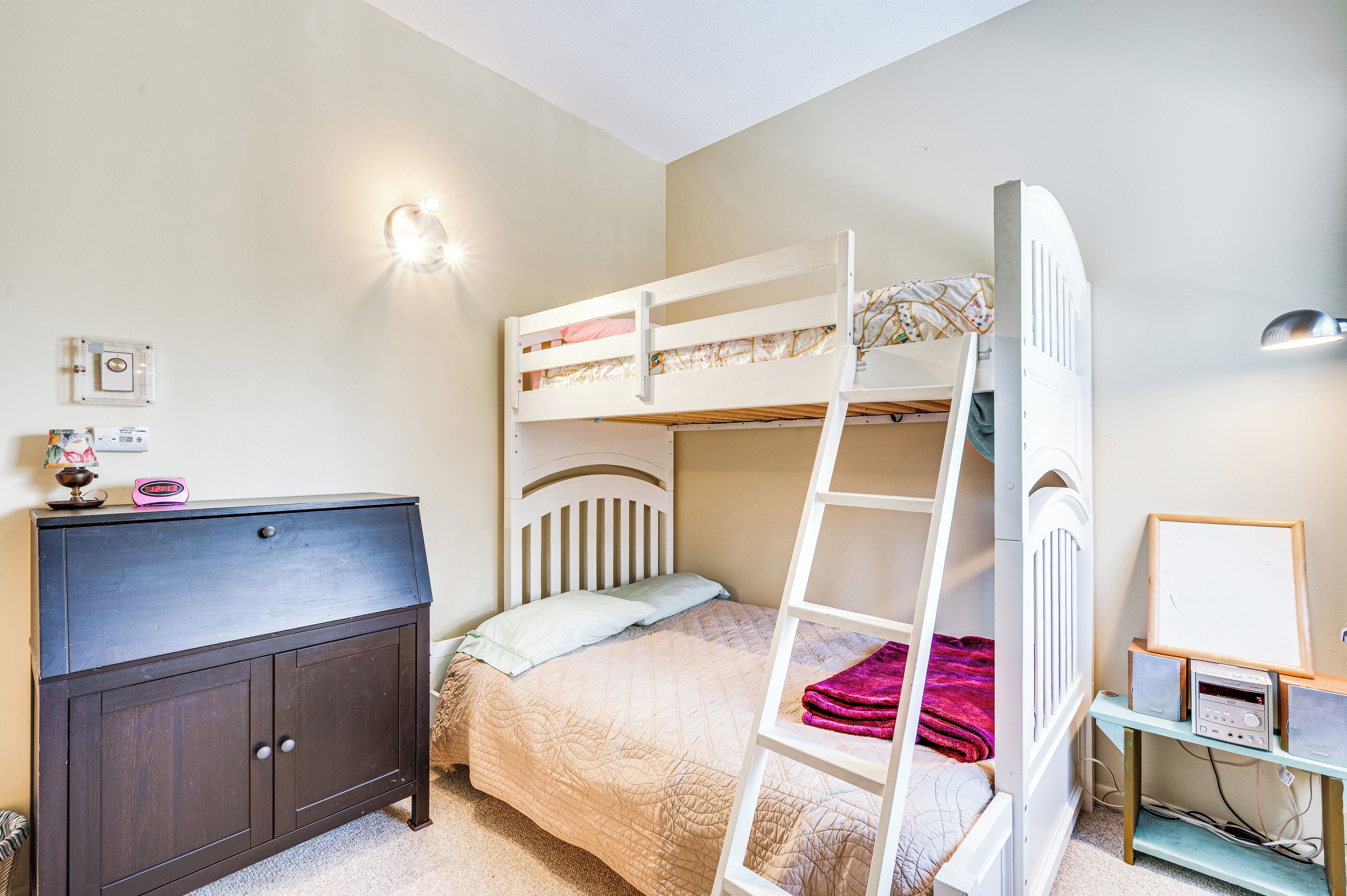A bunk bed with a ladder, a desk with a computer, and a cabinet.