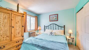 Een slaapkamer met een bed, een houten garderobe, een raam met gordijnen en een wanddecoratie.