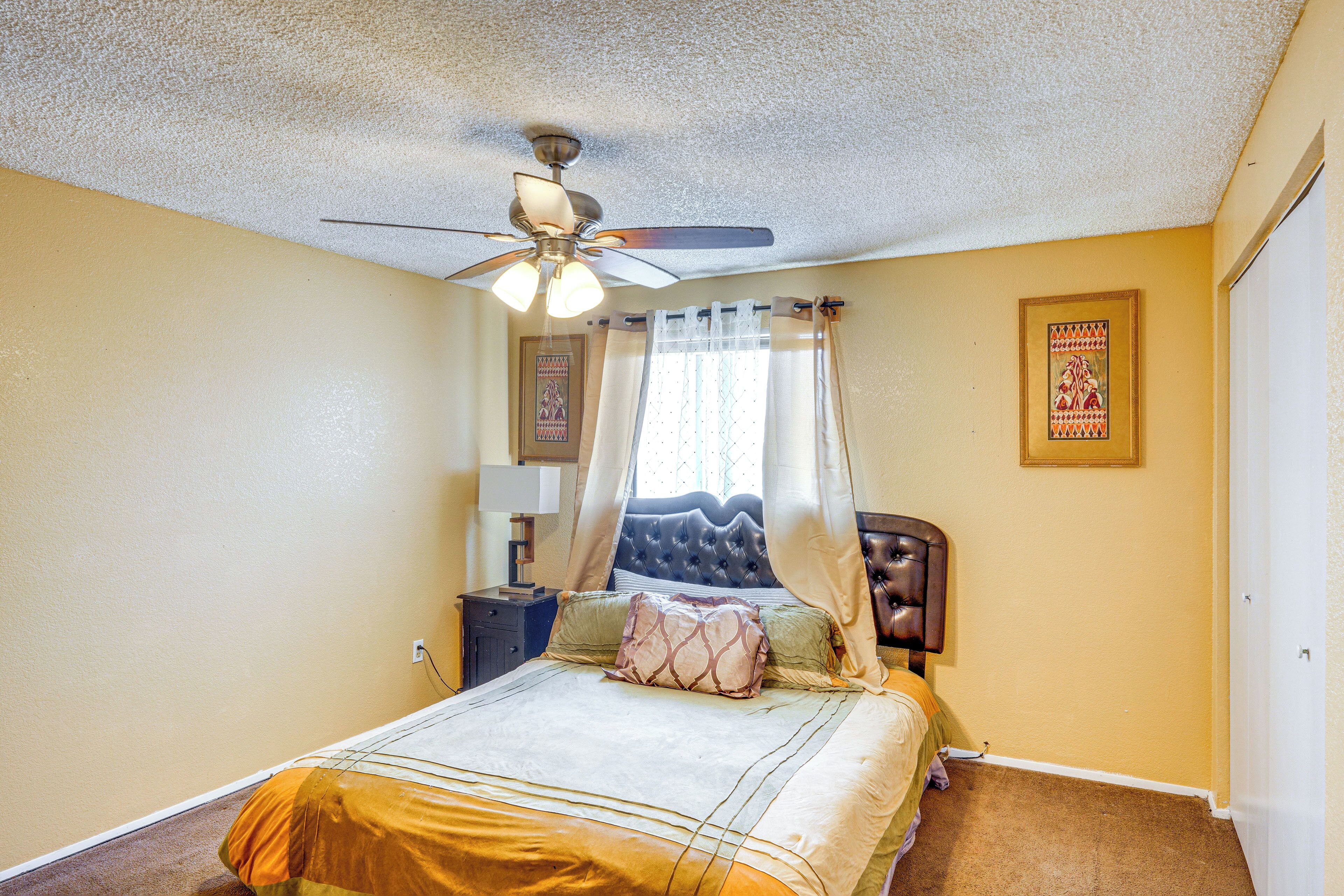 A bedroom with a bed, a ceiling fan, a nightstand, a lamp, and a framed picture on the wall.