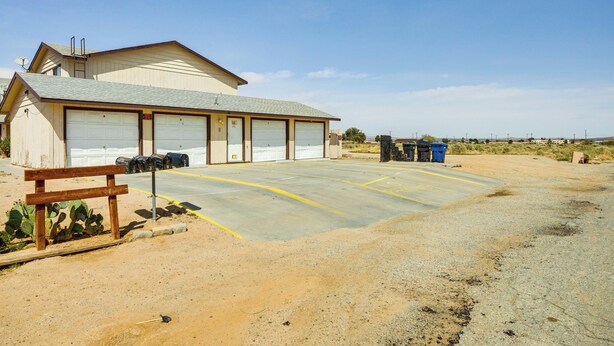 A single-story building with a garage, a paved parking area, and a cactus plant.