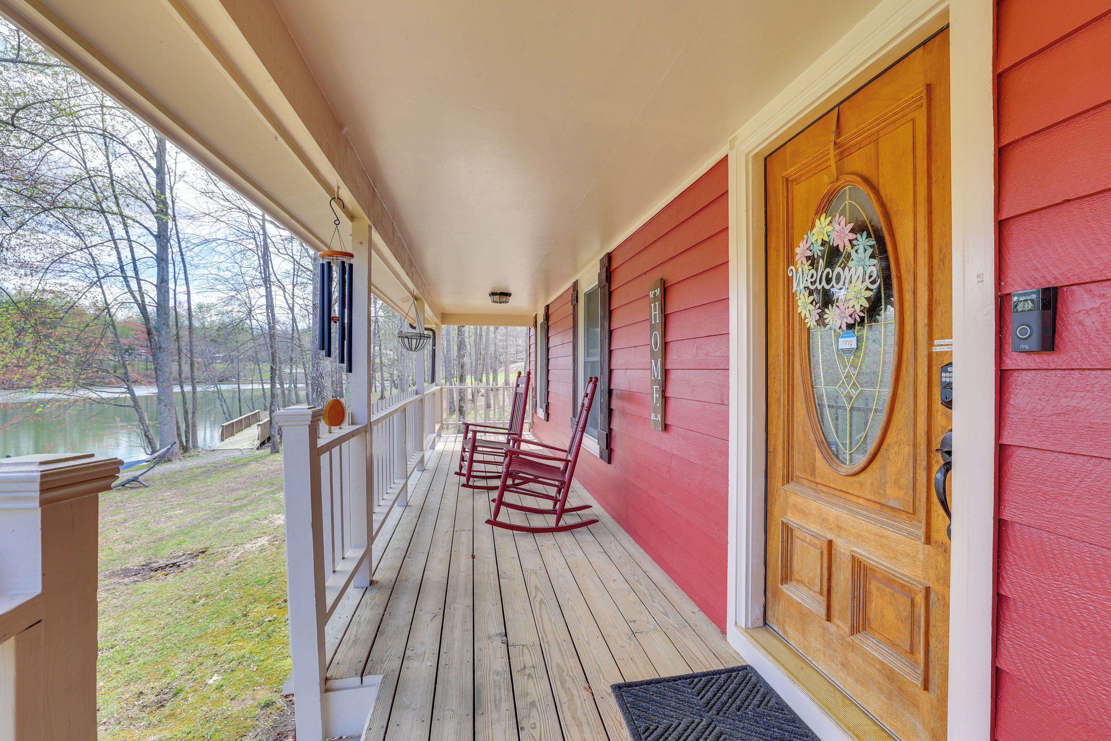 A wooden porch with rocking chairs, a welcome sign, and a view of a lake.