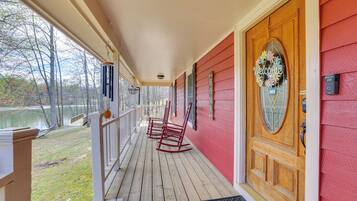 A wooden porch with rocking chairs, a welcome sign, and a view of a lake.