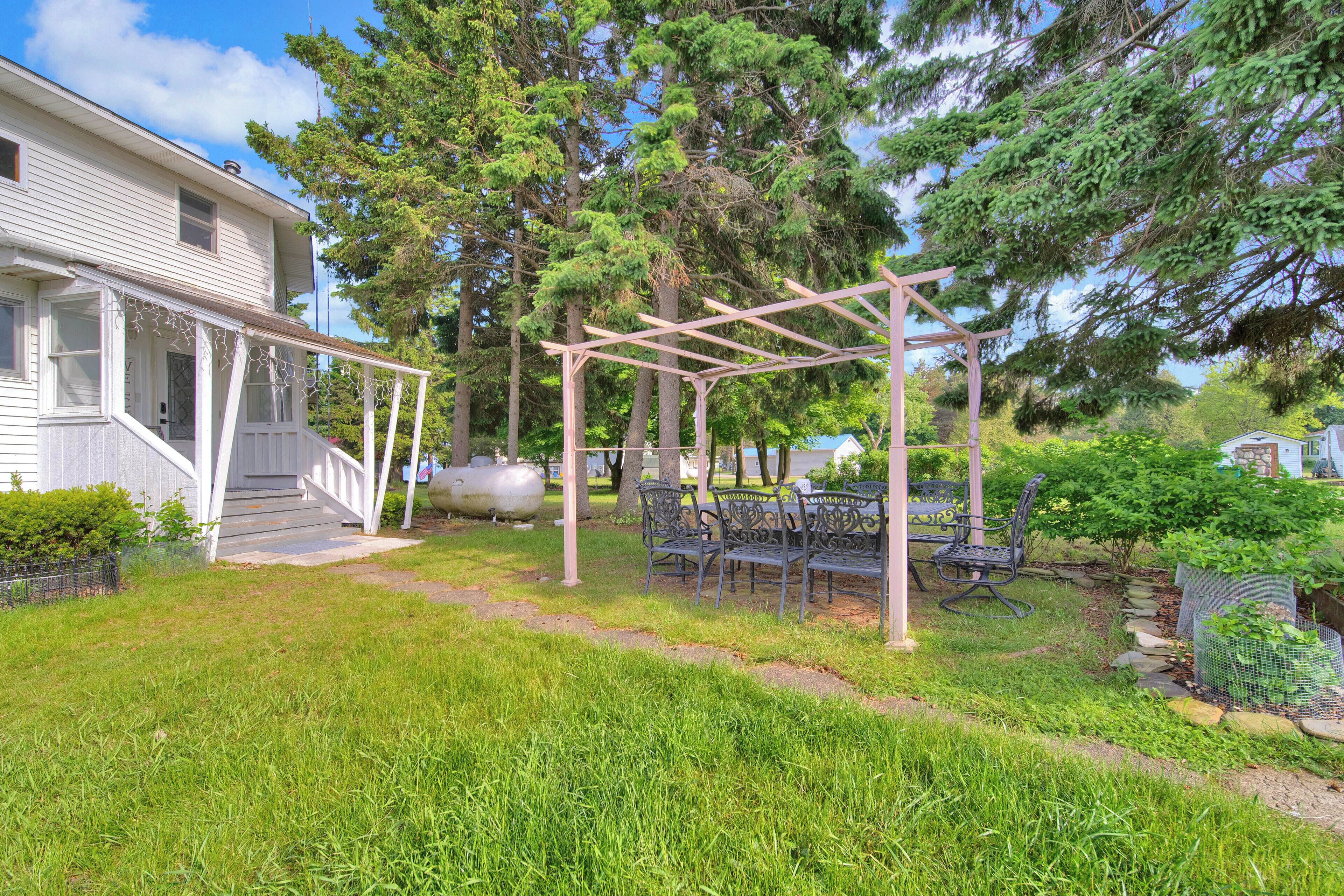 A covered patio with metal chairs and a swing set, surrounded by a grassy yard and trees.