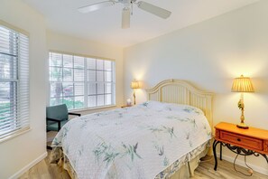 Un dormitorio con cama, dos lámparas de noche, una silla, ventilador de techo y ventana con persianas.