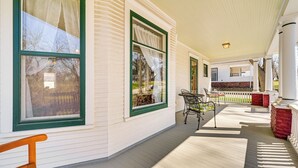 Une véranda couverte avec un plancher en bois, de grandes fenêtres à cadres verts et du mobilier d’extérieur.