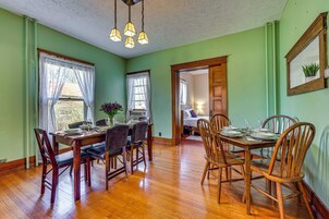 Comedor con mesa de madera dispuesta para cuatro comensales, rodeada de sillas, y un pasillo que conduce a un dormitorio.