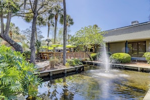 A serene outdoor area with a pond, a wooden deck, and a restaurant with outdoor seating. - Beautifully Updated Hilton Head Villa with Direct Ocean Views (Hilton Head Island)