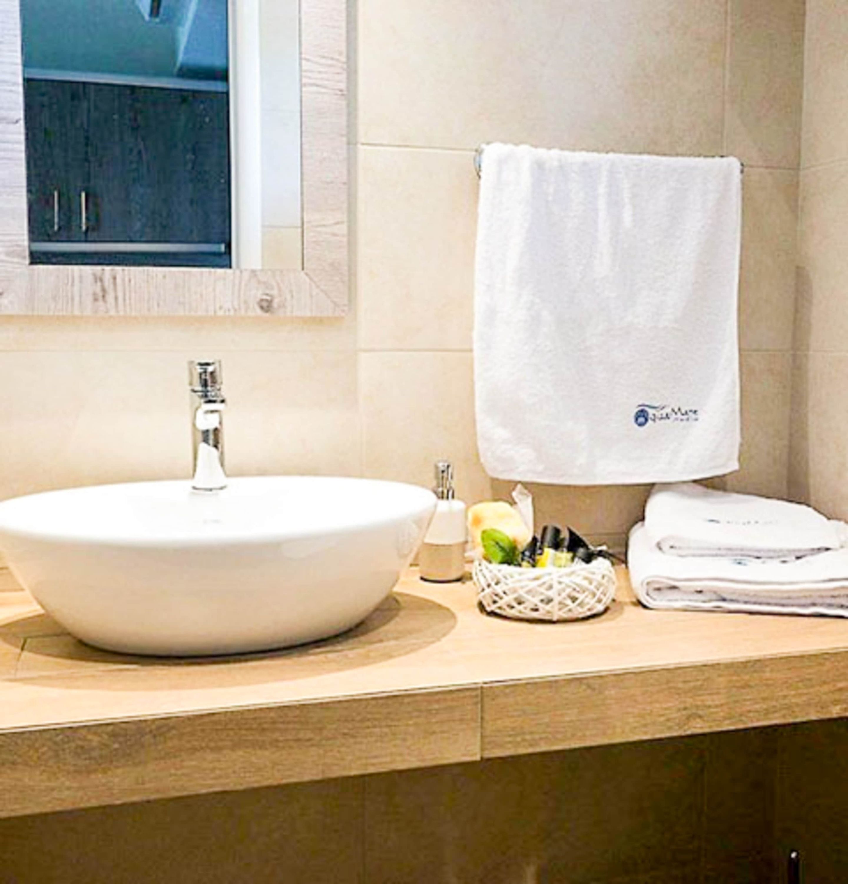 A bathroom with a round white sink, a towel hanging on the wall, and a basket with toiletries.