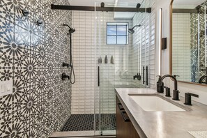 Ein modernes Badezimmer mit einer gläsernen Duschkabine, einem großen Spiegel und einem Waschbecken mit modernem Wasserhahn.