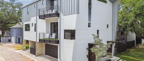 A modern two-story residential building with a balcony, a garage, and a well-maintained lawn.