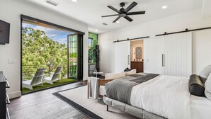 Une chambre moderne avec un grand lit, un ventilateur de plafond et une vue sur un balcon équipé de chaises.