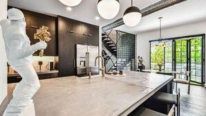 Une cuisine moderne dotée d’un grand îlot central, de meubles de rangement aux couleurs sombres et d’un escalier menant à l’étage supérieur.