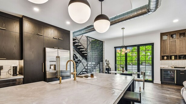 Une cuisine moderne avec des meubles en bois foncé, un grand îlot central, des appareils électroménagers en acier inoxydable et un escalier doté d’une rampe en métal.