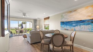 A spacious living area with a large window, a ceiling fan, and a dining table with chairs. - Unbeatable location with Ocean Views, sleeps 6 (St Simons Island)