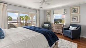 A bedroom with a large bed, a ceiling fan, a dresser, a chair, and a view of the beach. - Unbeatable location with Ocean Views, sleeps 6 (St Simons Island)