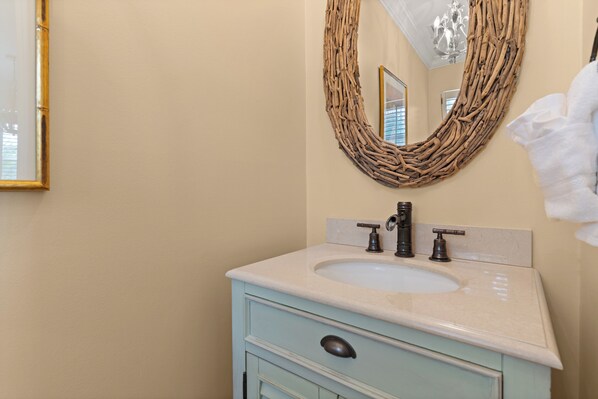 A bathroom with a light blue vanity, a white sink, and a mirror with a woven frame.