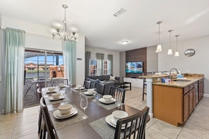 A modern kitchen with a central island, dining area with a table set for four, and a living area with a sofa and TV.