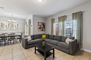 A living room with a sectional sofa, a dining table with chairs, and artwork on the walls.
