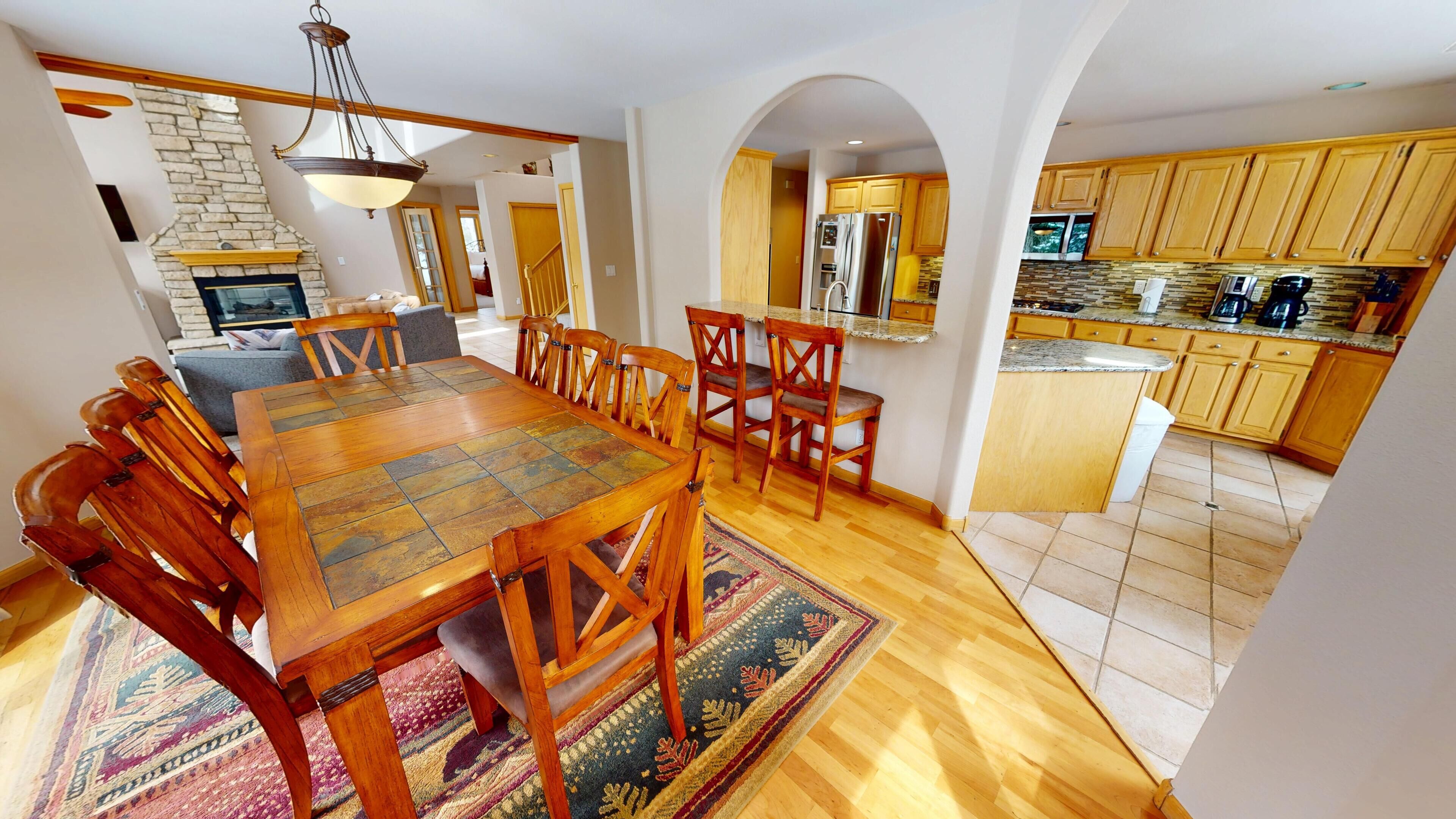 Un comedor amplio con una mesa y sillas de madera, una cocina con armarios de madera y salpicadero de piedra, y una chimenea de piedra.