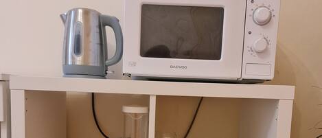 A white cabinet with a microwave, kettle, and various kitchen items.
