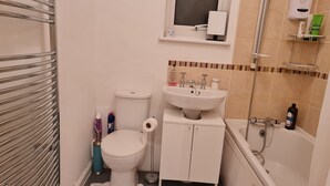 A bathroom with a toilet, sink, and bathtub. There is a towel rack, a shelf with toiletries, and a window above the sink. - KELVIN HOUSE (Ferryhill)