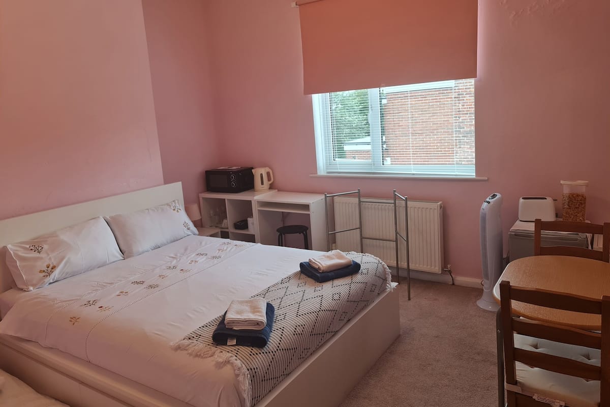 A bedroom with a bed, a desk, a chair, a radiator, and a window.