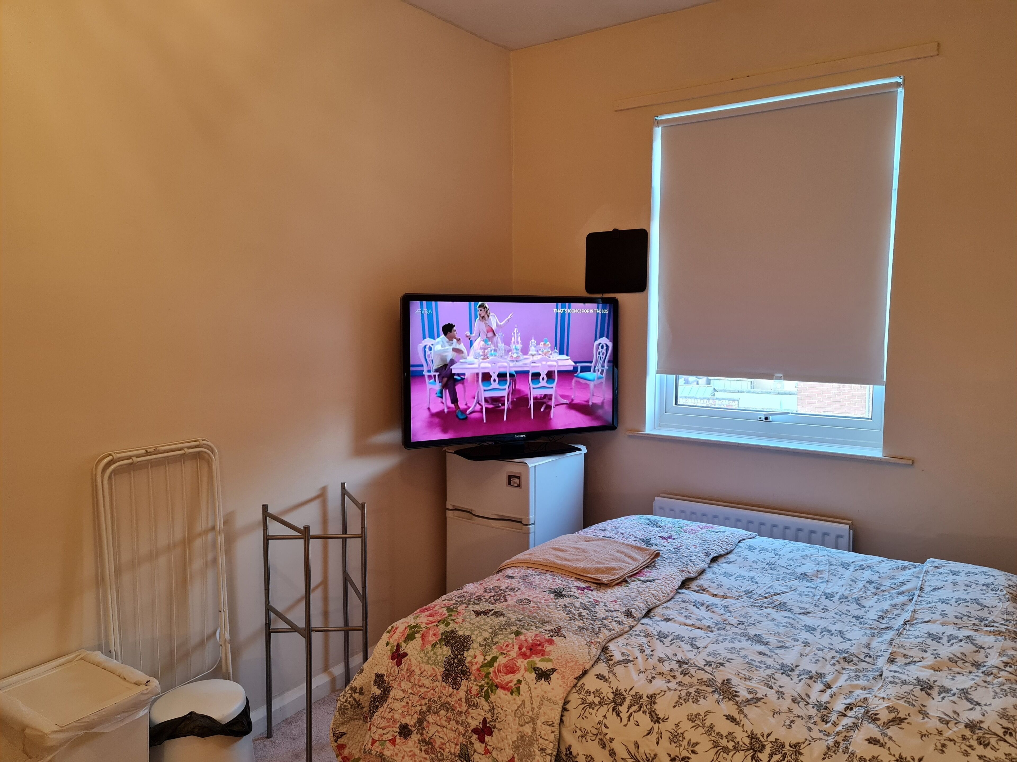 Habitación de hotel con cama, televisor sobre un mueble, radiador, ventana con persianas y radiador en la pared.