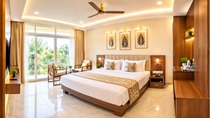 A hotel room with a large bed, a desk, a chair, a TV, and a balcony with a view of palm trees. - HOTEL THE PEARL SHINE (Gokarna)