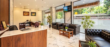 A hotel lobby with a reception desk, seating area, and large windows offering a view of the outdoors.