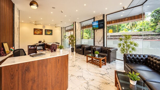A hotel lobby with a reception desk, seating area, and large windows offering a view of the outdoors. - HOTEL THE PEARL SHINE (Gokarna)