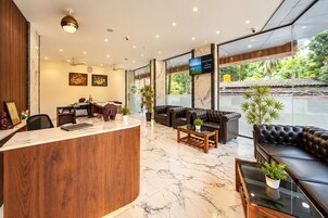 A hotel lobby with a reception desk, seating area, and large windows offering a view of the outdoors.