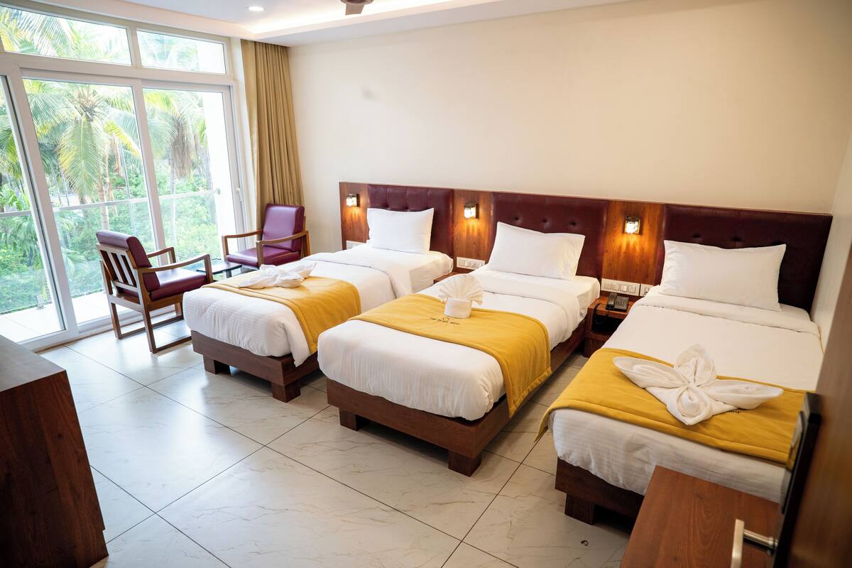 Ein Hotelzimmer mit drei Betten, einem Holztisch und einem Stuhl.