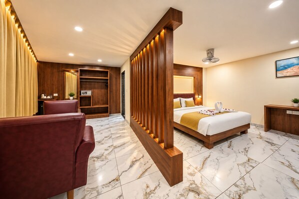 Quarto de hotel com cama, área de estar, escrivaninha e banheiro.
