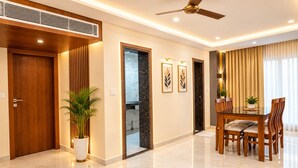A modern hotel room with a wooden door, a potted plant, a dining area with a table and chairs, and a ceiling fan. - HOTEL THE PEARL SHINE (Gokarna)