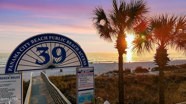 A beach entrance sign with palm trees and a sunset.