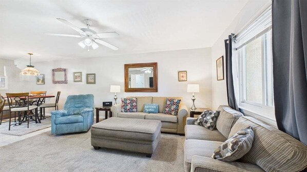 A living room with a sofa, armchair, ottoman, and a dining table with chairs. - Caye's Cove 132-Walk to Beach-Sleeps 6 (Panama City Beach)