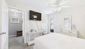 A bedroom with a bed, a dresser, a vanity with a mirror, a television mounted on the wall, and a ceiling fan. - Caye's Cove 132-Walk to Beach-Sleeps 6 (Panama City Beach)