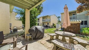 An outdoor patio with stone tables and chairs, a covered grill, and a pergola with an umbrella. - Caye's Cove 132-Walk to Beach-Sleeps 6 (Panama City Beach)