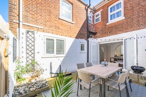 A patio with a table and chairs, a barbecue grill, and a small garden area with rocks and plants. - 12 Hans Place, Cromer, Norfolk (Cromer)