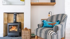 A cozy living room with a wood-burning stove, a striped armchair, a wicker basket, and a shelf with decorative items. - 12 Hans Place, Cromer, Norfolk (Cromer)