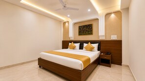 Une chambre d’hôtel moderne, dotée d’un grand lit, d’une table de chevet, d’un ventilateur de plafond et d’une œuvre d’art accrochée au mur.