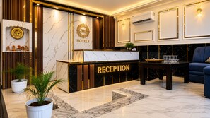 A reception area with a marble reception desk, a blue sofa, and a potted plant. - Hotel Paradise International by JMD Group (New Delhi)