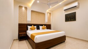 A bedroom with a wooden bed, white bedding, and a yellow throw. - Hotel Paradise International by JMD Group (New Delhi)