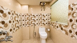 A bathroom with a toilet, shower, and a wall with a circular pattern. - Hotel Paradise International by JMD Group (New Delhi)