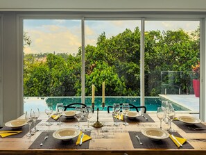 A dining table set for six with a view of a swimming pool and lush greenery.