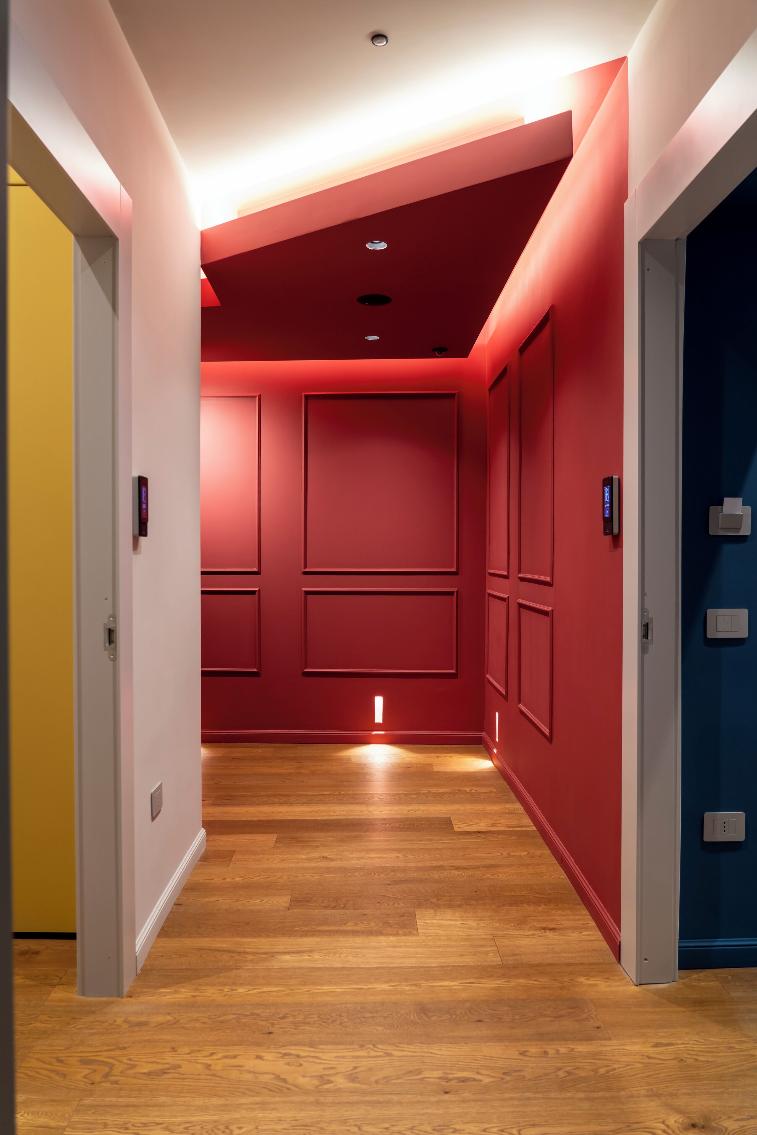 Un couloir aux murs rouges, doté d’un plancher en bois et d’un éclairage encastré.