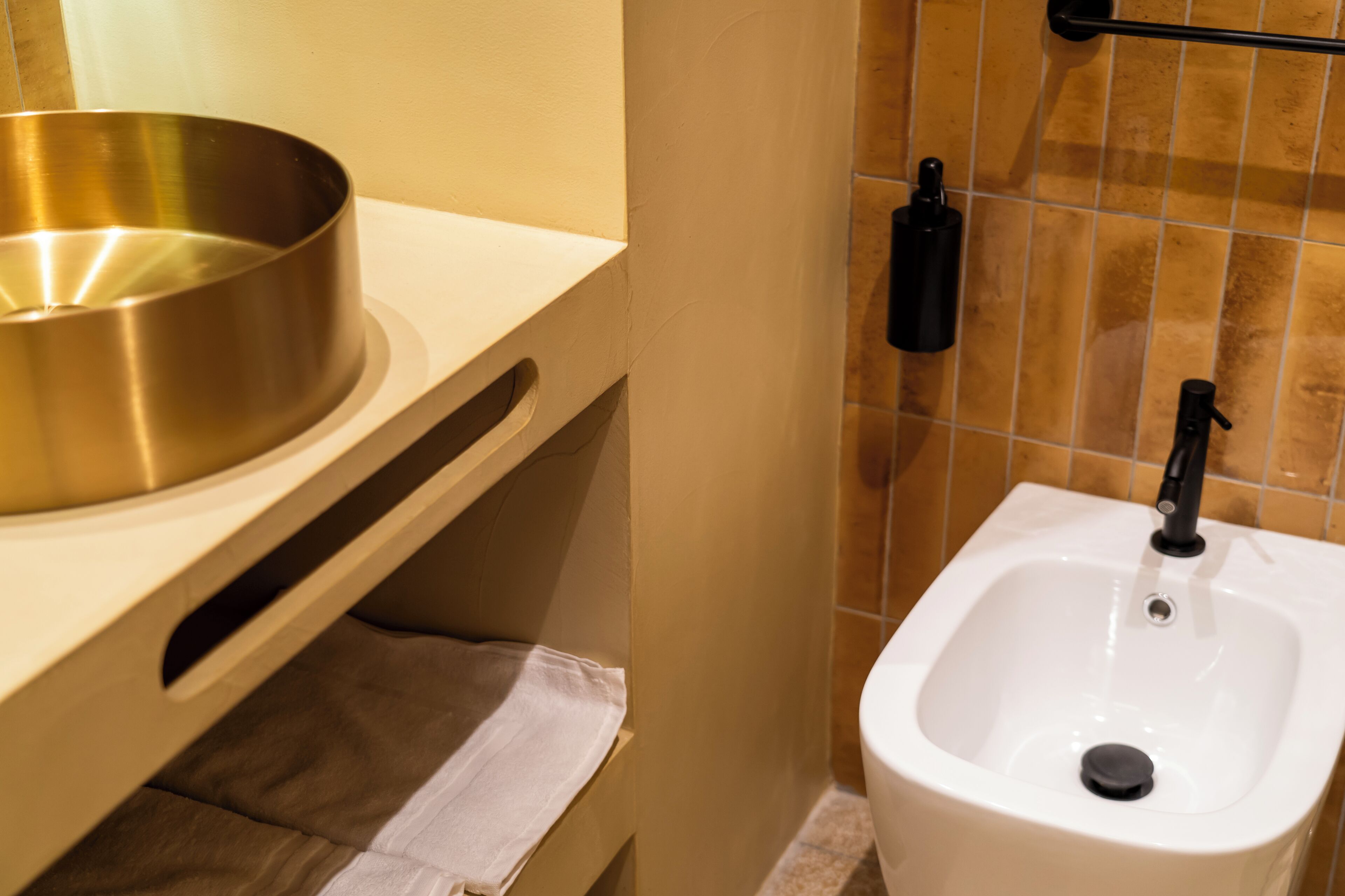 A bathroom with a white sink, a gold basin, and a towel rack.