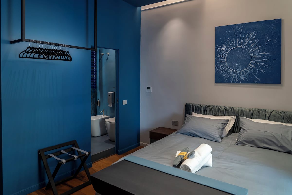 A modern bedroom with a bed, a nightstand, a mirror, and a bathroom visible through an open door.