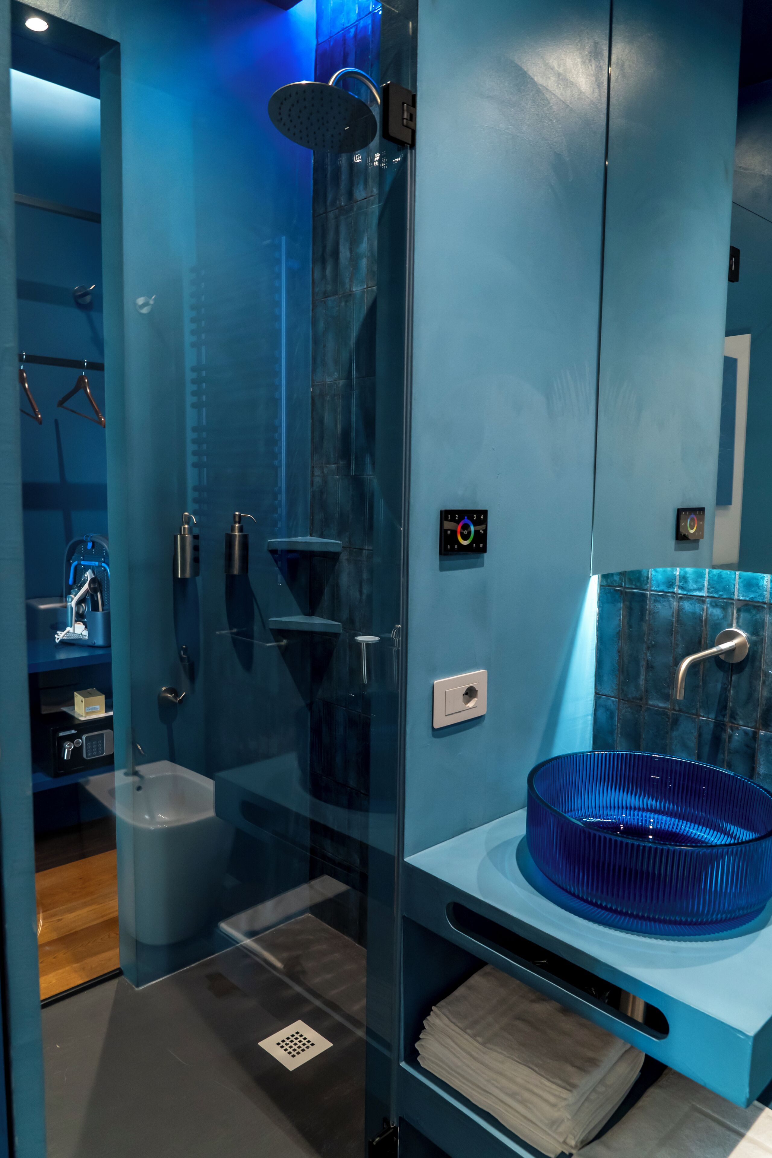 A modern bathroom with a glass-enclosed shower, a blue sink, and a towel rack.