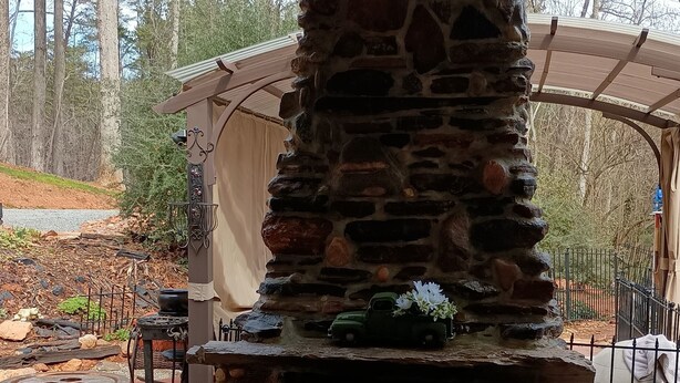 A stone-built outdoor fireplace with a chimney, surrounded by a stone base and a metal fence.